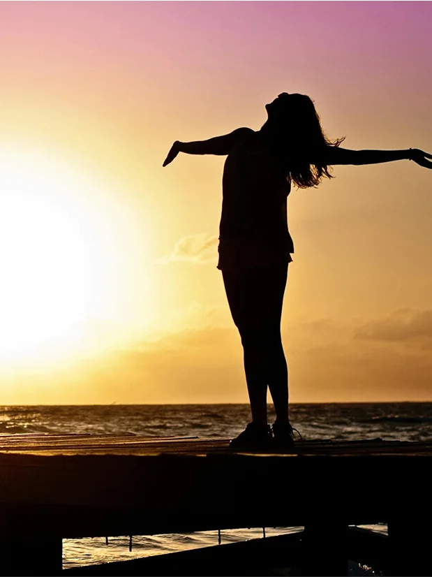 truma-therapy4 Silhouette of a person with outstretched arms facing a sunset over the ocean.