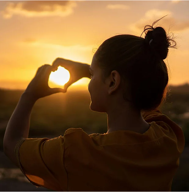 truma-therapy7 Silhouette of a person forming a heart shape with their hands around the setting sun